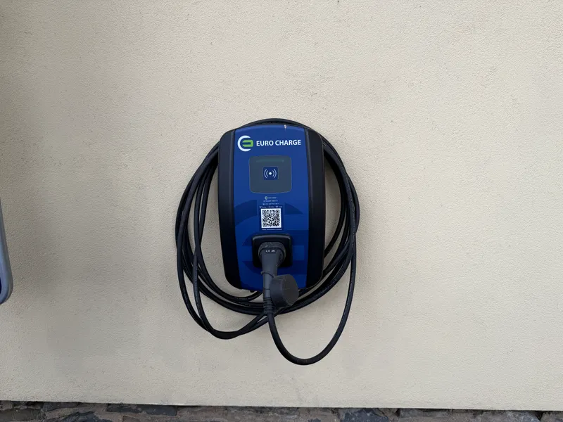 Detail modrého wallboxu EURO CHARGE s kabelem na světlé zdi